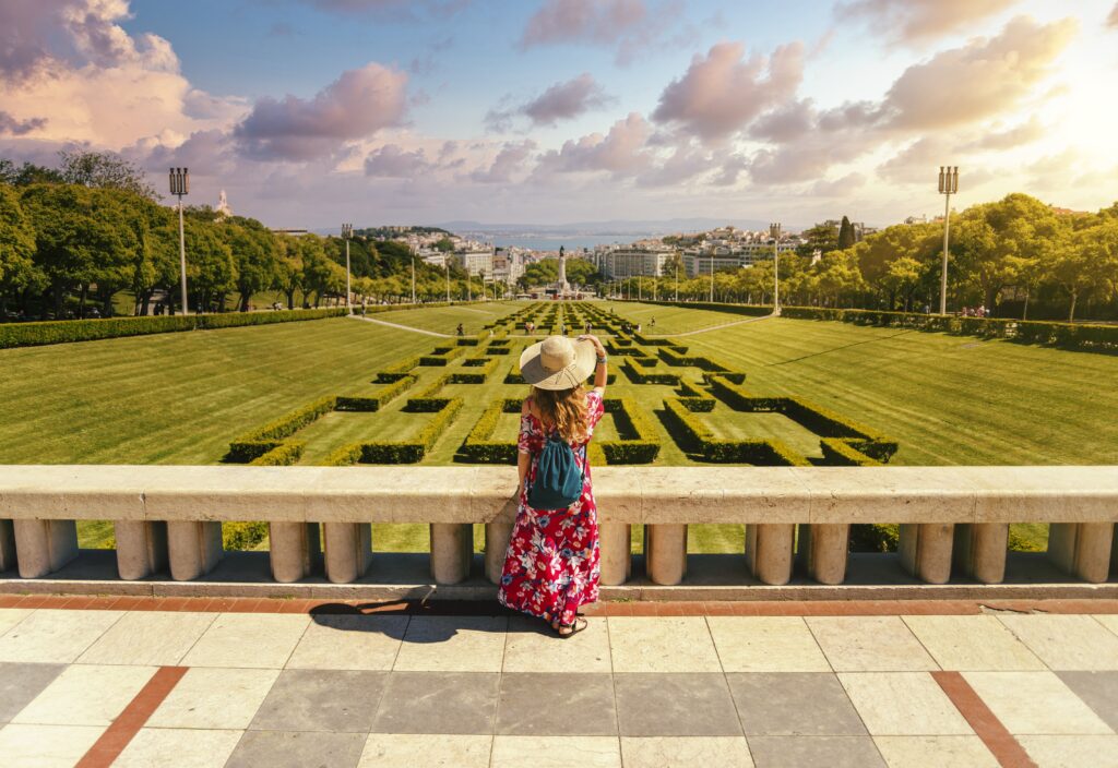 Young female tourist in a red floral dress in The Eduardo VII Park under the sunlight in Portugal
